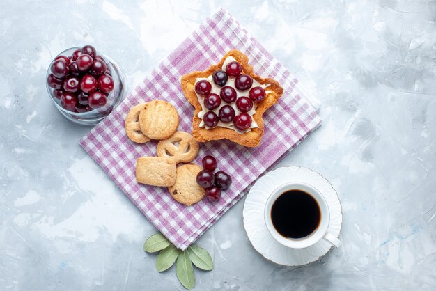 Top view of fresh sour cherries inside plate with star shaped creamy cake and cookies on white desk, fruit sour summer cake biscuit