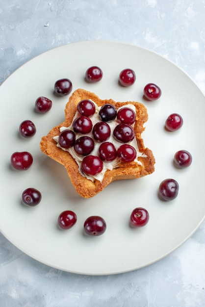 Top view of fresh sour cherries inside plate with star shaped creamy cake on light, fruit sour berry vitamine summer