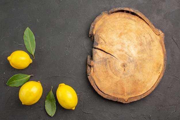 Вид сверху свежие кислые лимоны с листьями на темном столе фруктов, лайма, желтых цитрусовых