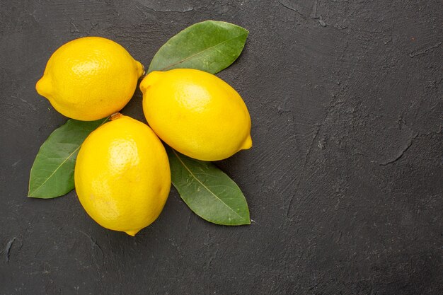 Top view fresh sour lemons with leaves on dark table lime yellow citrus fruits