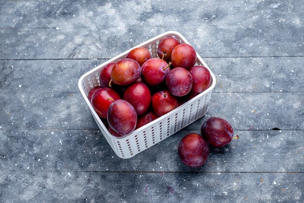 Top view of fresh sour plums inside white basket on grey floor fruit fresh sour mellow ripe