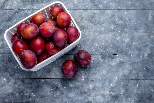 Top view of fresh sour plums inside white basket on grey, fruit fresh sour mellow