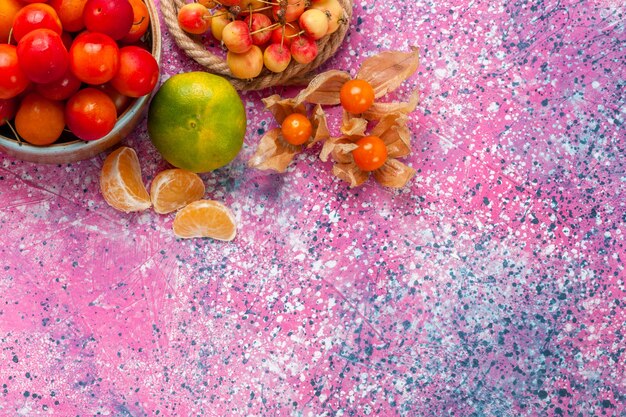 淡いピンクの机の上の小さなプレートの中に新鮮な酸っぱいプラムのまろやかな果物の上面図。