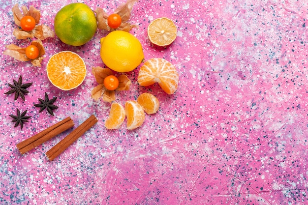 Вид сверху свежие кислые мандарины с лимонами и корицей на розовом фоне.