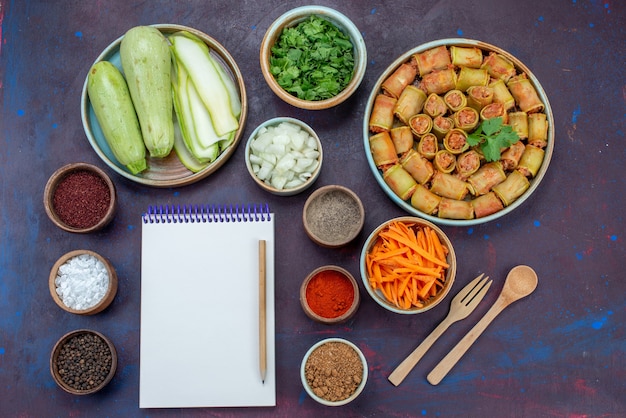 Top view fresh squashes with greens and seasonings meat rolls and notepad on the dark-purple desk meat dinner vegetable meal