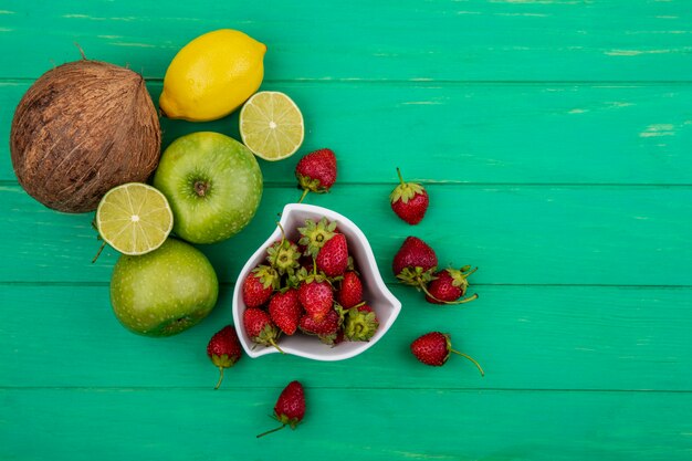 Top view of fresh strawberries on a bowl with coconu tapples lime on a green wooden background with copy space