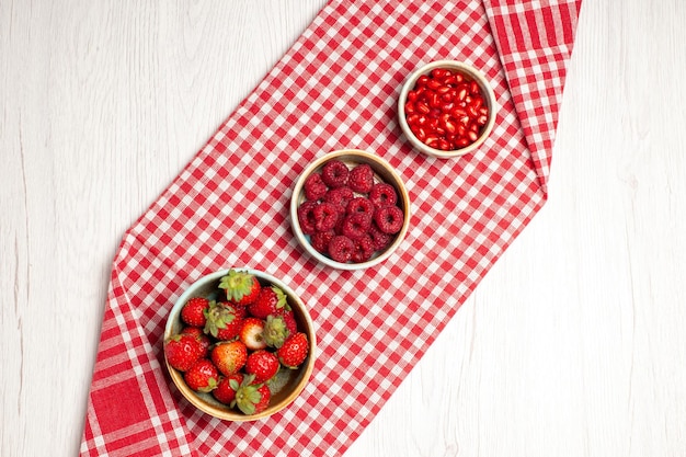 Free photo top view fresh strawberries with raspberries and pomegranates on a white desk berry fresh fruits mellow ripe wild