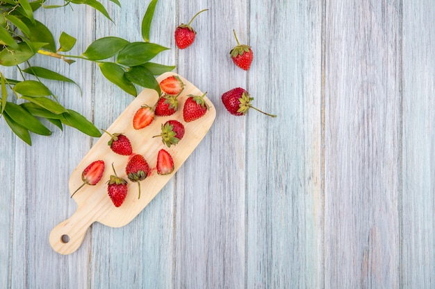 Top view of fresh strawberries on a wooden kitchen board with leaves on a grey wooden background with copy space