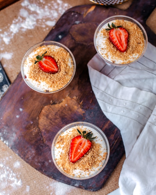 Free photo top view fresh strawberry dessert inside little glasses on the brown wooden desk