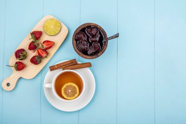 Top view of fresh strawberry on a wooden kitchen board with a strawberry jam on a wooden bowl on a blue background with copy space