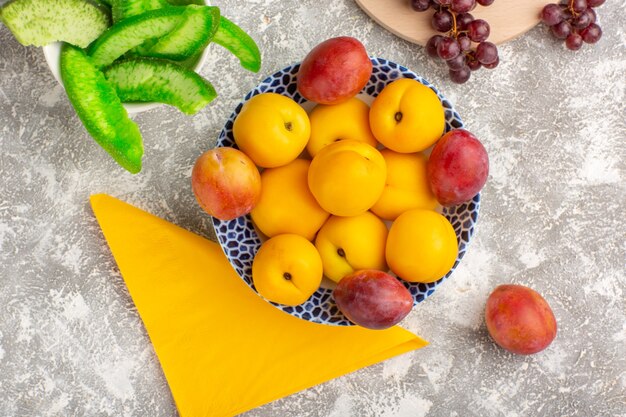 Top view fresh sweet apricots yellow fruits inside plate with plums and grapes on white desk