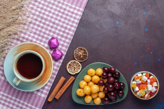 Top view of fresh sweet cherries inside plate with tea cinnamon and candies on dark surface