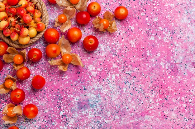 淡いピンクの机の上に梅と新鮮な甘いサクランボの上面図。