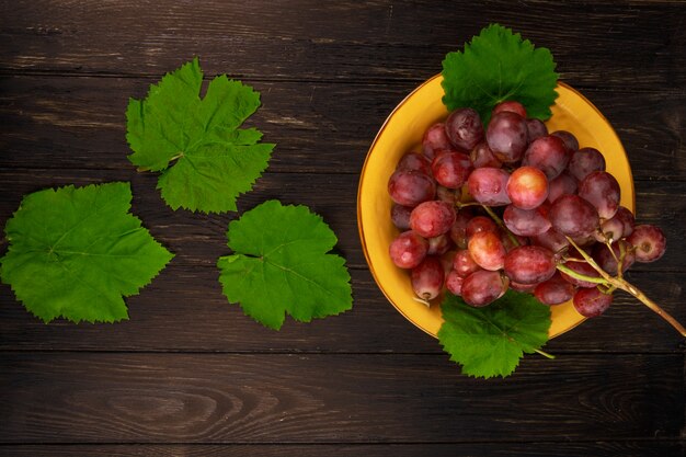 Top view of fresh sweet grape in a plate and green grape leaves on dark wooden table