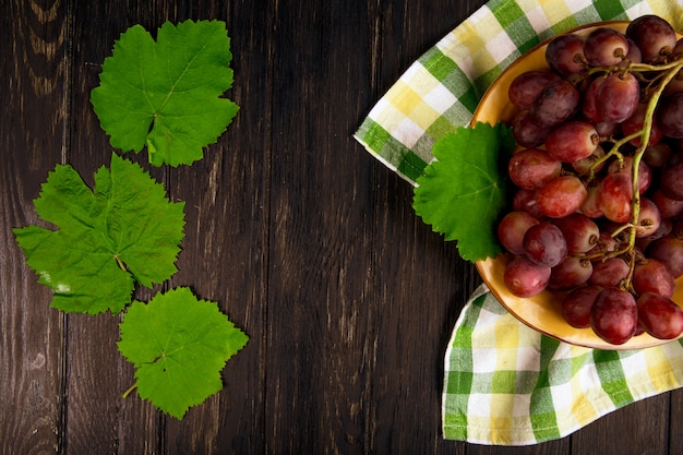 Top view of fresh sweet grape in a plate with green grape leaves on dark wooden table with copy space