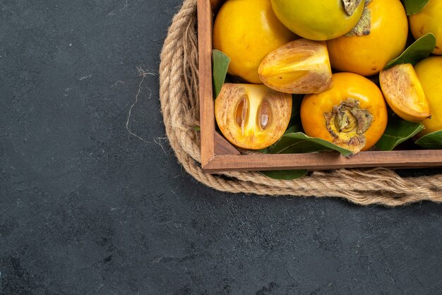 Вид сверху свежей сладкой хурмы внутри коробки на темном столе со вкусом спелых фруктов