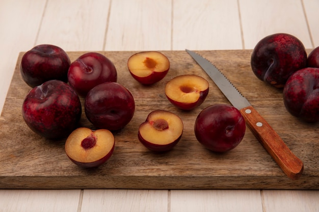 Top view of fresh and sweet pluots on a wooden kitchen board with knife on a beige wooden wall