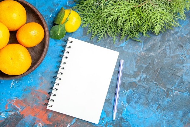 Top view fresh tangerines inside plate with notepad on blue background