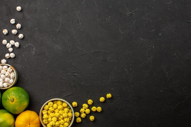 Top view of fresh tangerines with candies on black-grey