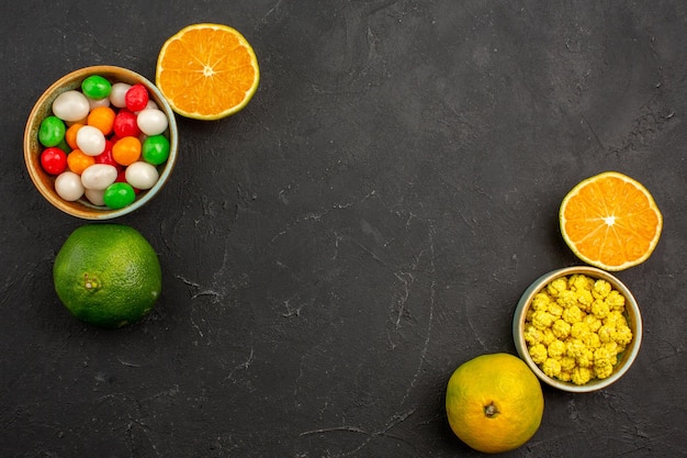 Top view of fresh tangerines with candies on black table