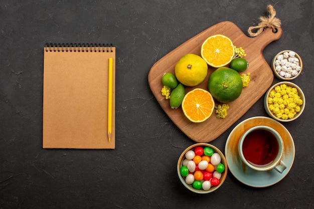 Top view of fresh tangerines with cup of tea and candies on black