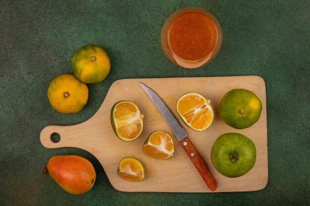 Top view of fresh tangerines on a wooden kitchen board with knife with tangerine juice on a glass