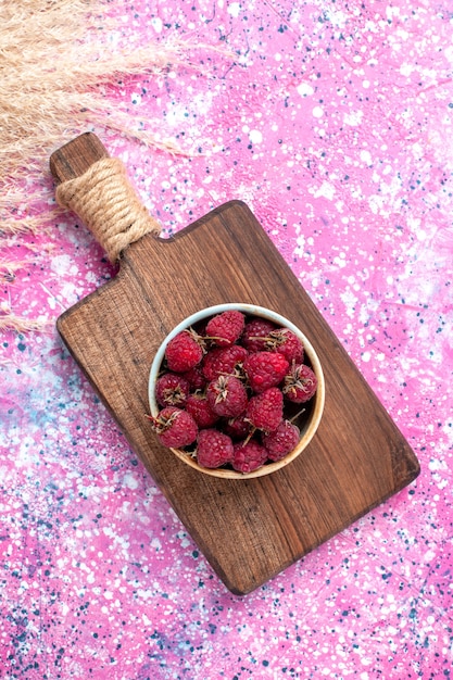 Top view of fresh tasty raspberries inside white plate on pink surface