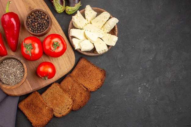 Top view of fresh tomatoes with dark. bread loafs and white cheese on black