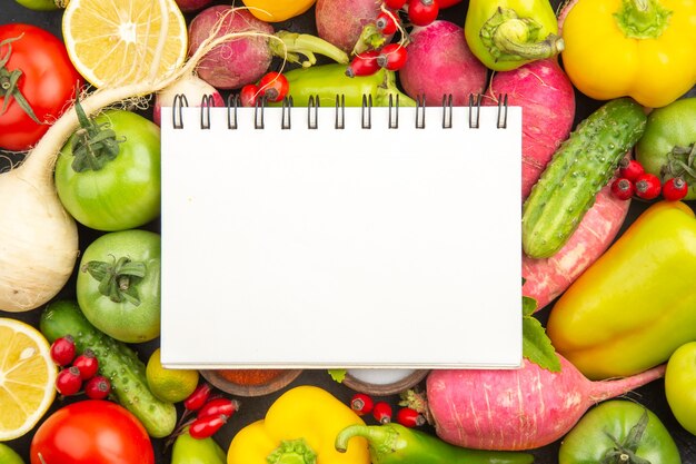 Top view fresh vegetable composition with seasonings and notepad on dark background