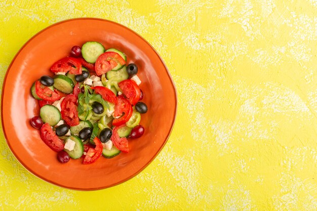 Вид сверху салат из свежих овощей с нарезанными огурцами помидоры оливковое внутри тарелка на желтом фоне овощная еда салат еда цветная фотография