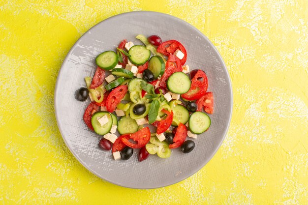 Top view fresh vegetable salad with sliced cucumbers tomatoes olive inside plate on yellow surface vegetable food salad meal color snack