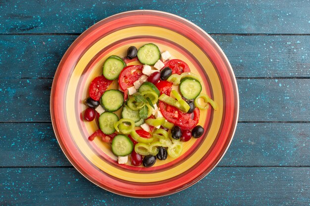 Top view fresh vegetable salad with sliced cucumbers tomatoes olive and white cheese inside plate with tomatoes on the dark-blue surface vegetable food salad meal snack