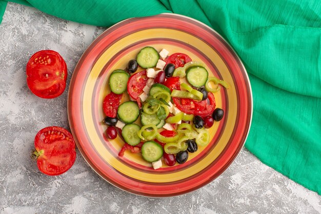 Top view fresh vegetable salad with sliced cucumbers tomatoes olive and white cheese inside plate with tomatoes on the grey surface vegetable food salad meal snack