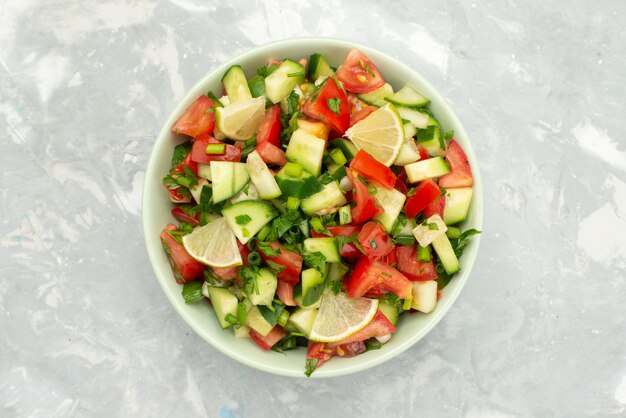 Вид сверху салат из свежих овощей с нарезанными овощами и дольками лимона внутри круглой пластины на синем