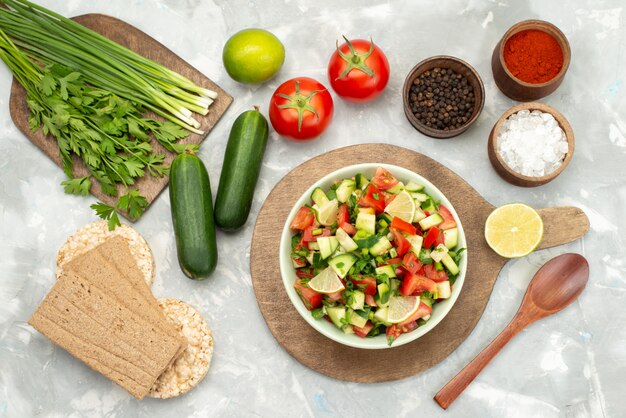 Top view fresh vegetable salad with sliced vegetables and lemon slices inside round plate with crisps on blue