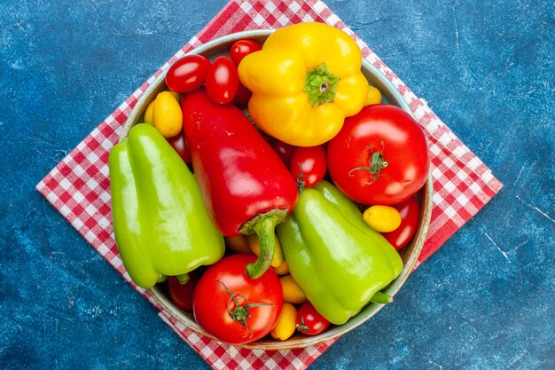 Top view fresh vegetables cherry tomatoes different colors bell peppers tomatoes cumcuat on platter on red white checkered kitchen towel on blue surface