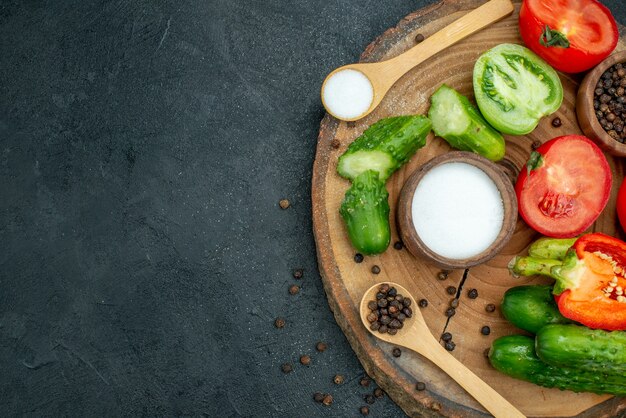 Top view fresh vegetables chopped cucumber black pepper and salt in wooden spoon on wood board on dark background