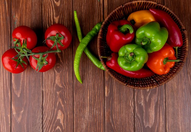 Top view of fresh vegetables colorful bell peppers red chili peppers in a wicker basket and fresh ripe tomatoes on wood rustic