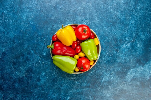 Top view fresh vegetables different colors bell peppers tomatoes cherry tomatoes in bowl on blue table with copy space