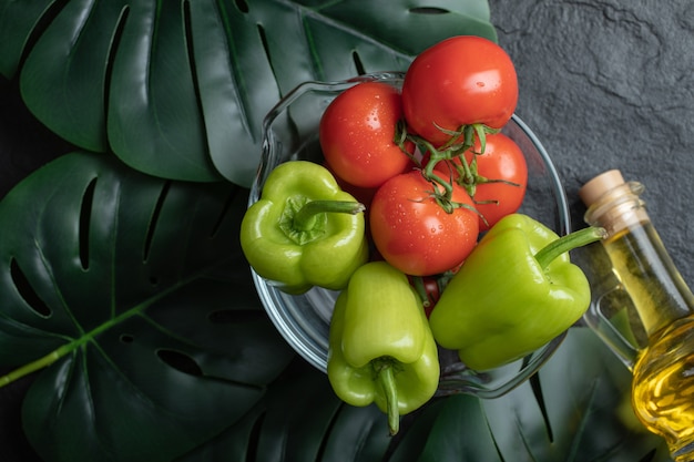 Top view of fresh vegetables in glass bowl and bottle of oil. 