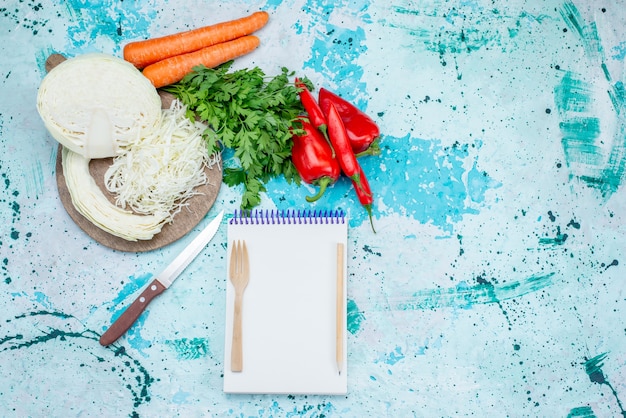 Free photo top view of fresh vegetables greens sliced cabbage carrots and peppers with notepad on bright-blue, food meal vegetable lunch healthy salad