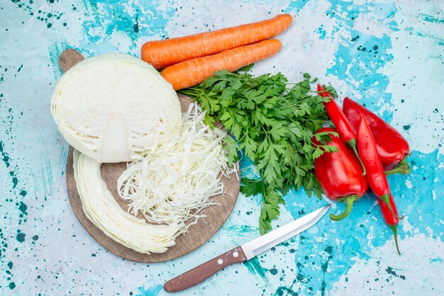 Top view of fresh vegetables greens sliced cabbage carrots and spicy hot peppers on bright-blue, food meal vegetable lunch healthy salad