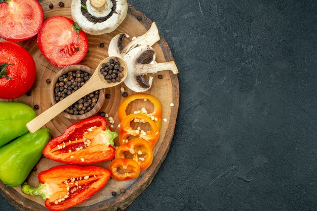 Top view fresh vegetables mushroom black pepper in bowl wooden spoon red tomatoes bell peppers on wood board on dark background