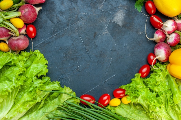 Top view fresh vegetables radish lemon green onion cherry tomatoes lettuce on dark surface with copy place