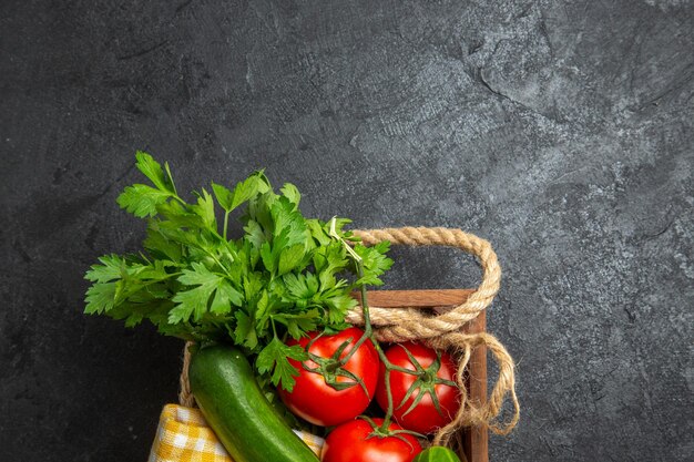 Top view of fresh vegetables red tomatoes cucumbers and squashes with greens on dark grey surface