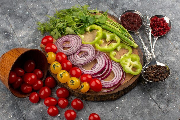 вид сверху нарезанные свежие овощи, такие как лук зеленый перец, красные и желтые помидоры на коричневом столе и серый