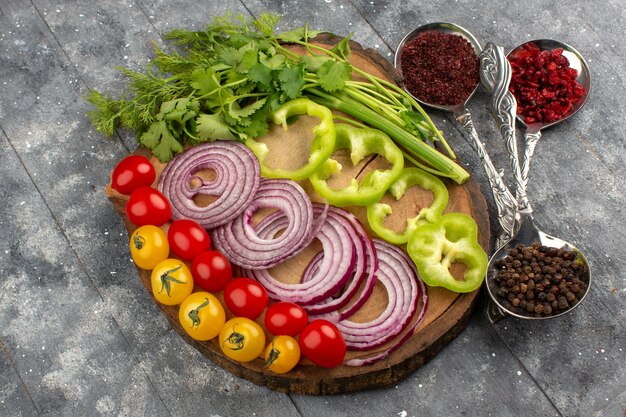 top view fresh vegetables sliced and whole such as yellow red tomatoes and onions on the brown desk on the grey