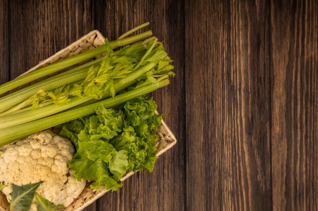 Top view of fresh vegetables such as celery lettuce and cauliflower on a bucket on a wooden wall with copy space