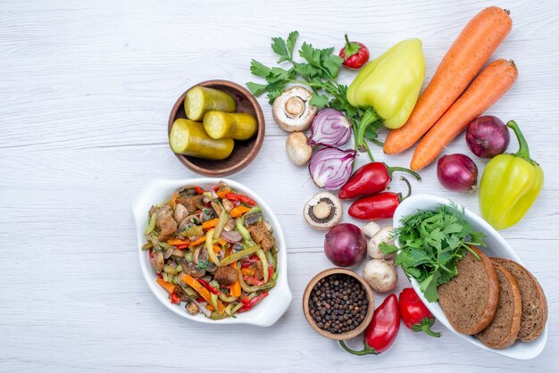 Top view of fresh vegetables such as pepper carrot onions with bread loafs and sliced meat dish on light desk, vegetable food meal vitamine