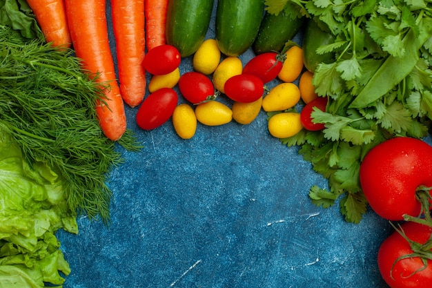 Top view fresh vegetables tomato parsley lettuce dill carrot cucumber cumcuat cherry tomatoes on blue background